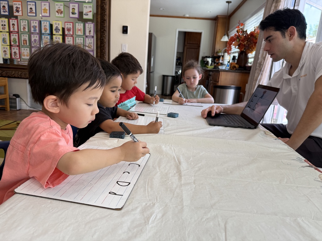 Children practicing letter formation on whiteboards while a teacher guides the lesson
