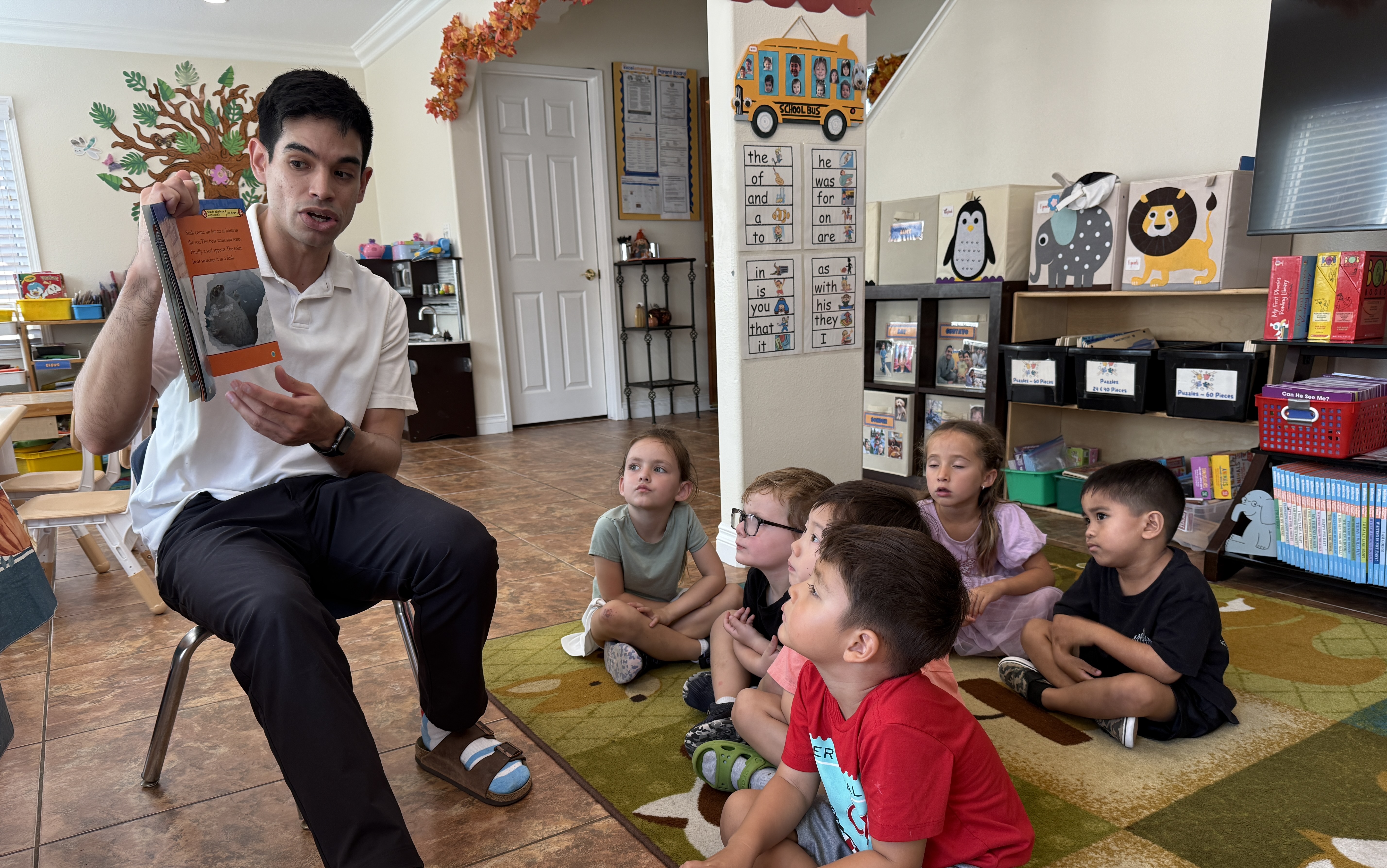 A teacher reading a nonfiction book aloud to children seated on the rug